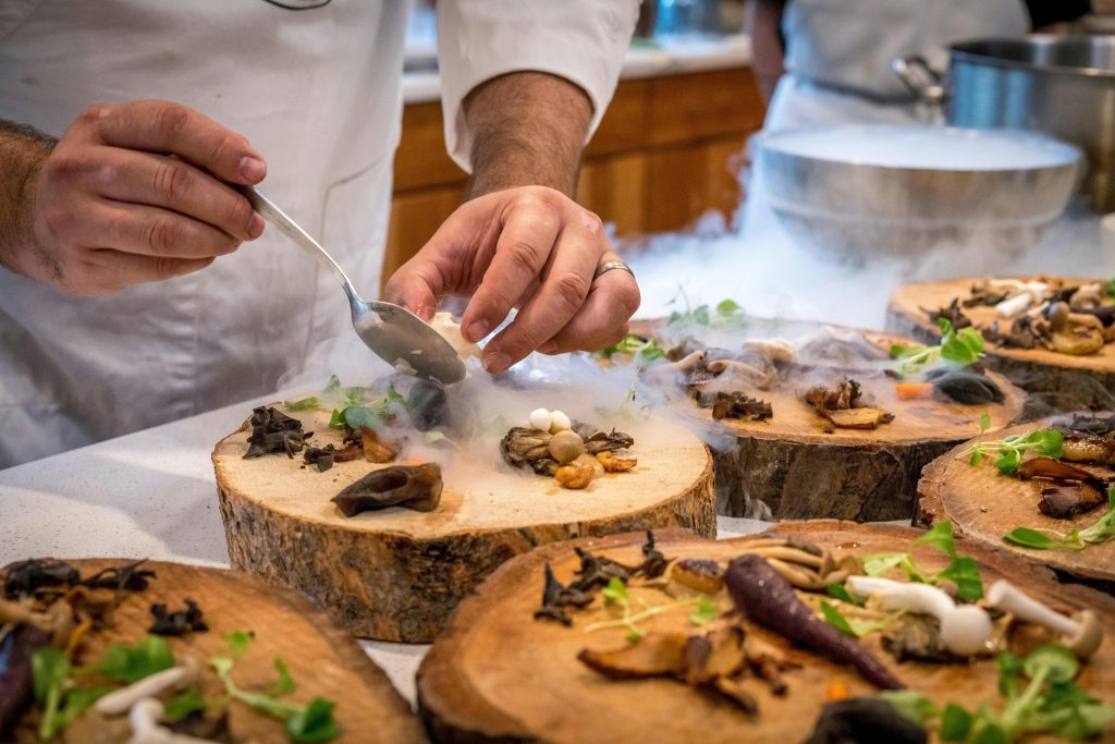 Chef dressant un plat gastronomique aux champignons et herbes sur rondins de bois.